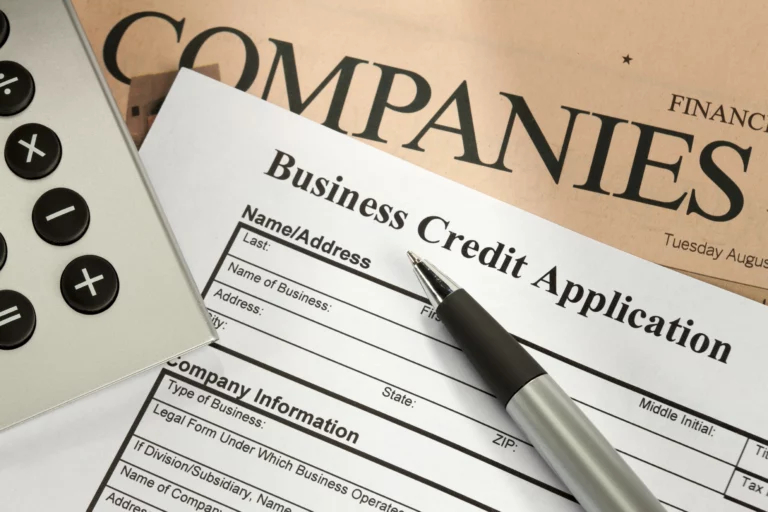 Business credit application form on table with pen and nearby calculator, newspaper titled “COMPANIES” partially visible — symbolizing rebuilding business credit after bankruptcy.