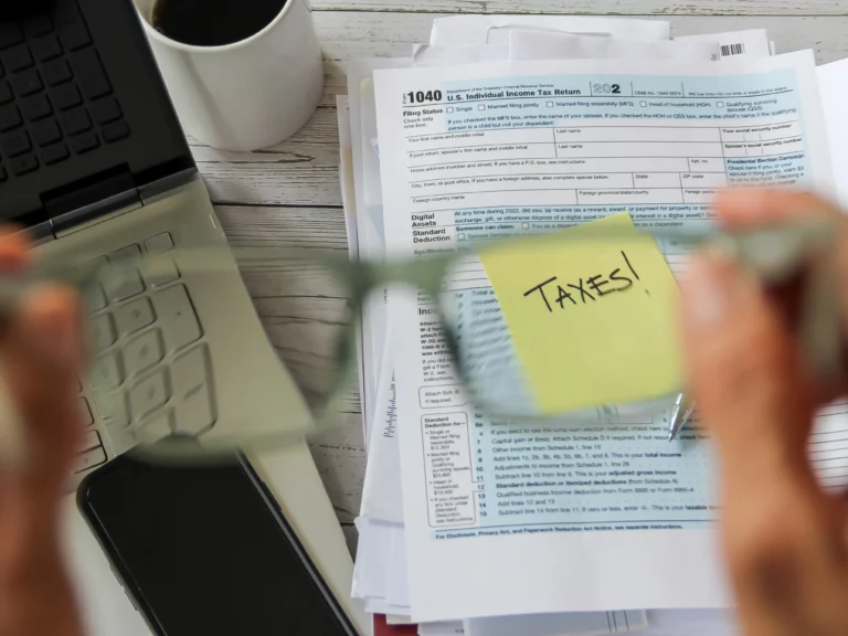 Sticky note labeled “TAXES!” placed on a 1040 tax form with calculator, laptop, smartphone, and coffee, symbolizing tax refund concerns during Chapter 7 bankruptcy in Missouri.