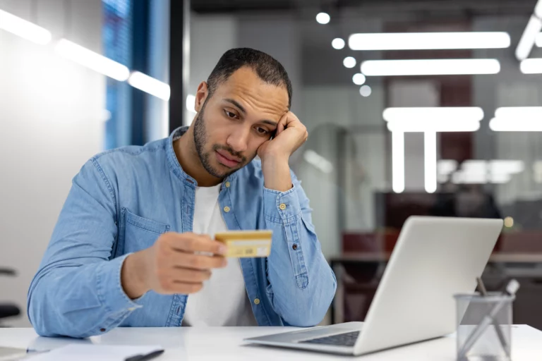 Concerned man reviewing a credit card statement beside a laptop in a home office, representing the financial stress and credit concerns many individuals face when considering Chapter 7 bankruptcy in Missouri.